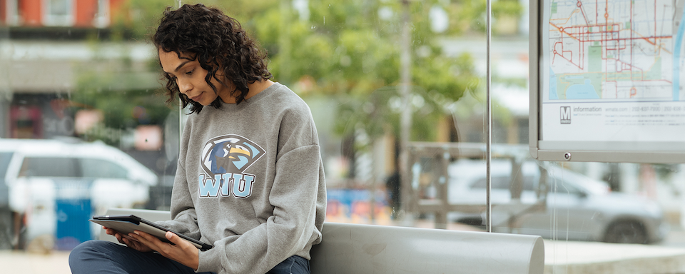 A Capital One Students and Grads associate sits on a bench with her iPad wearing her college's sweatshirt
